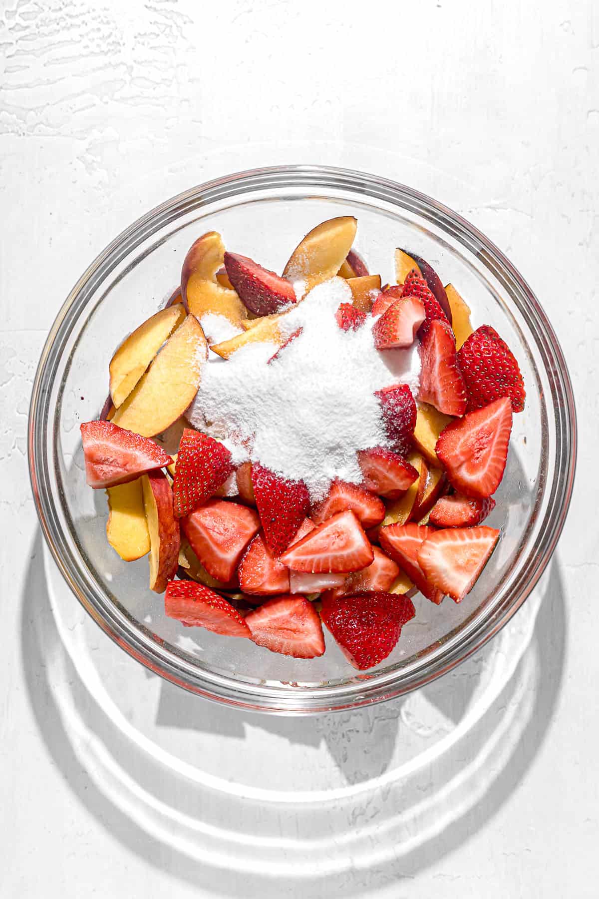 strawberries, peaches, and sugar in glass bowl.