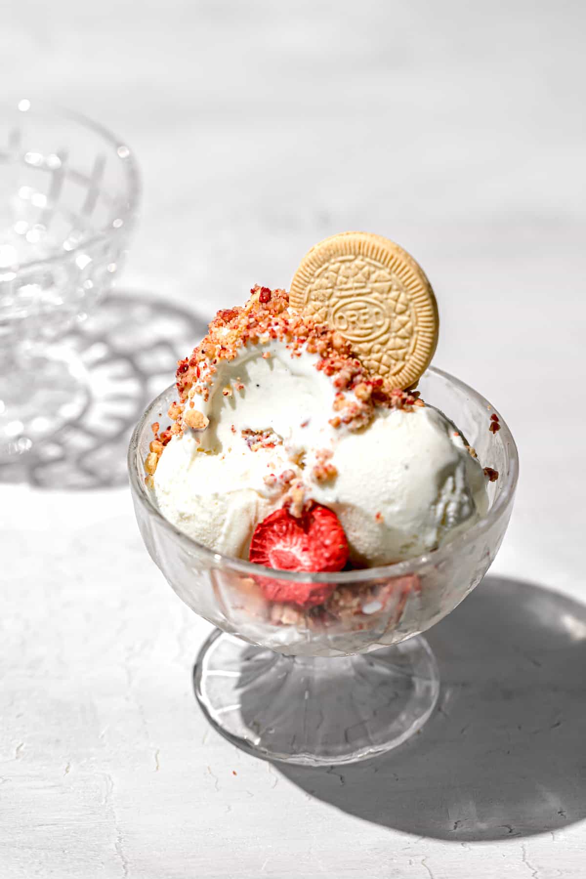 vanilla ice cream topped with strawberry shortcake crumble and golden oreo in glass bowl.