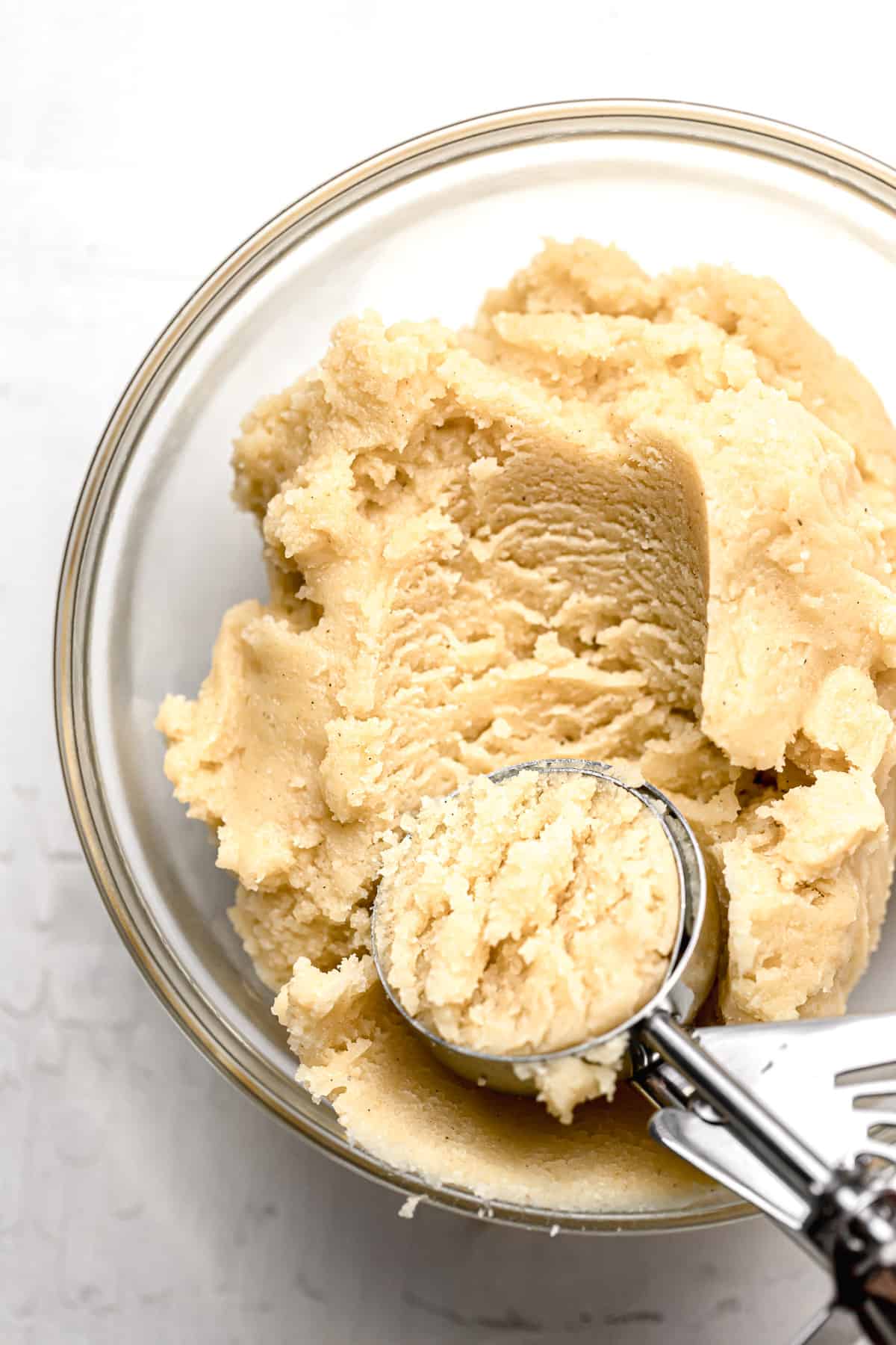 snickerdoodle cookie dough in glass bowl with cookie scoop