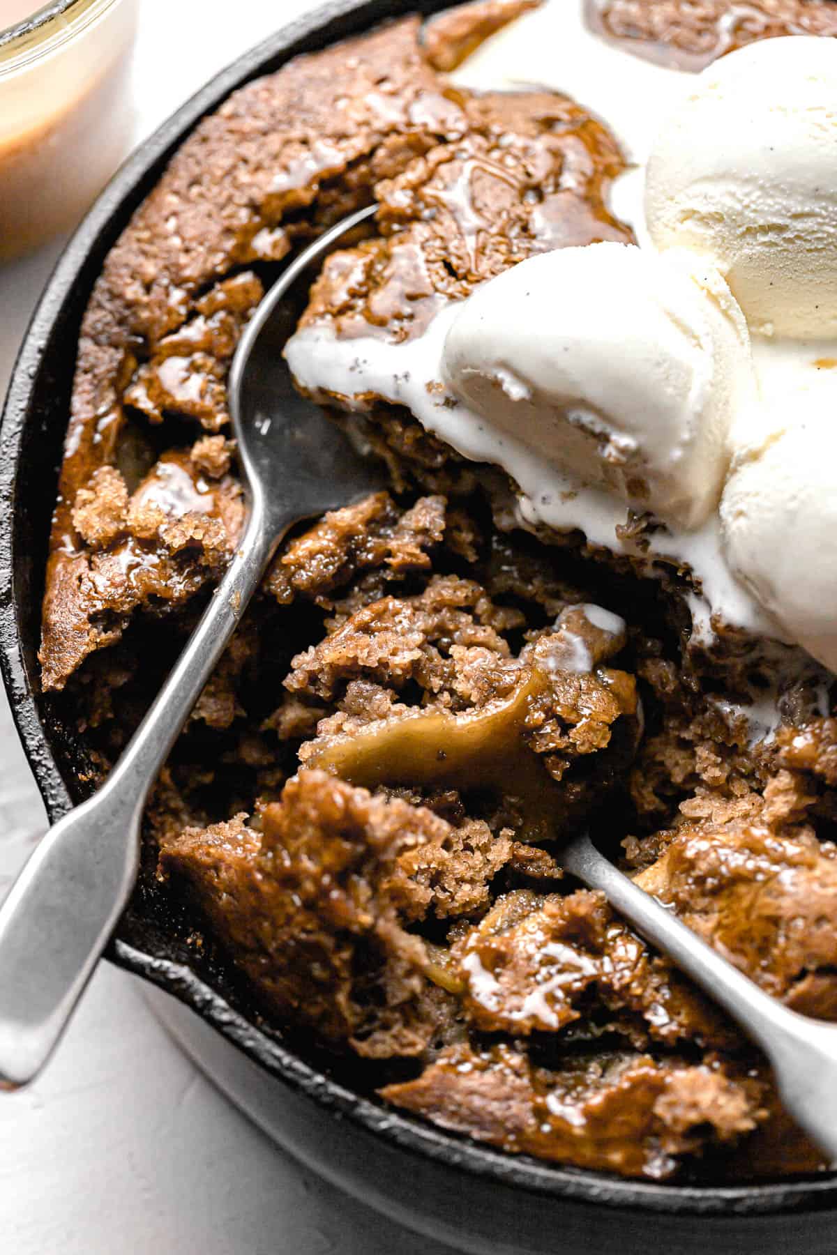 caramel apple dump cake in cast iron with ice cream and two spoons