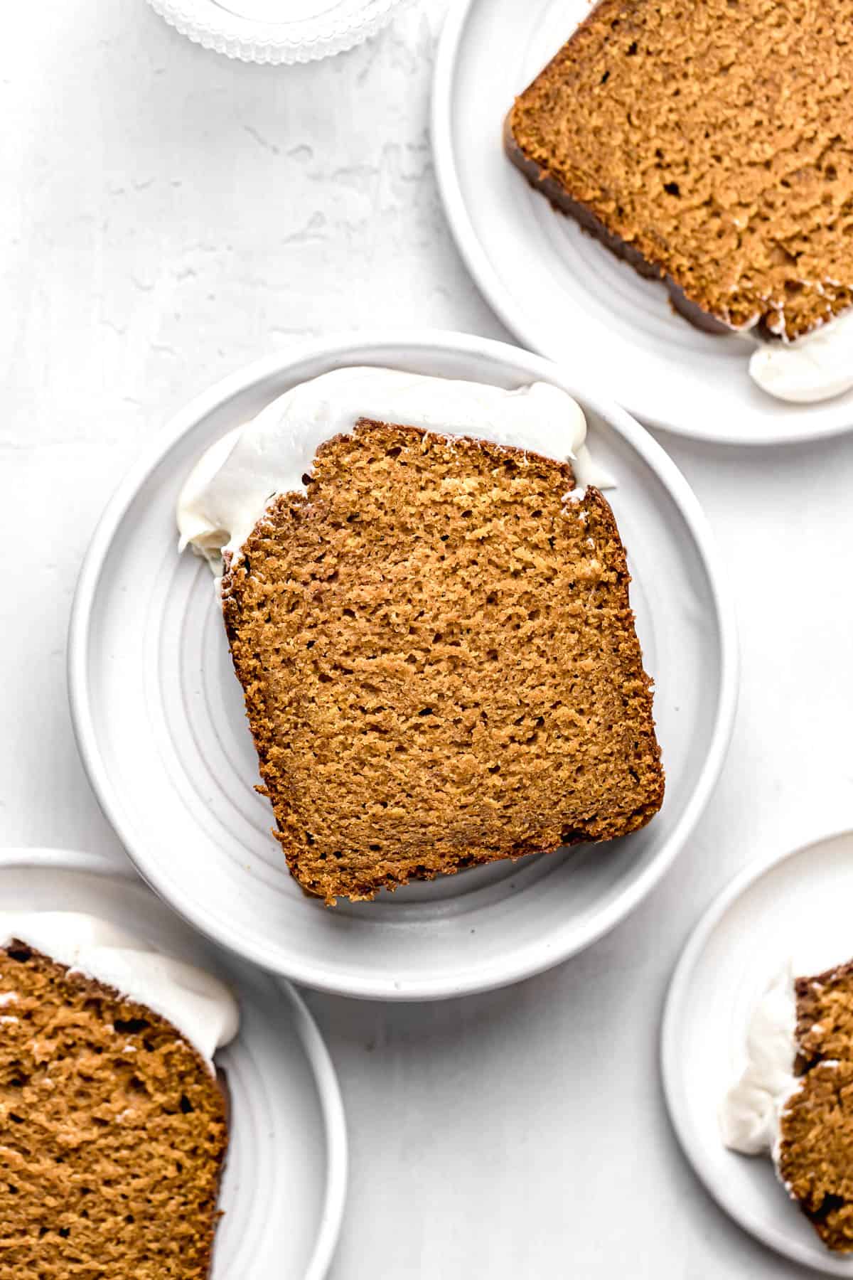slices of pumpkin bread with cream cheese frosting on white plates.