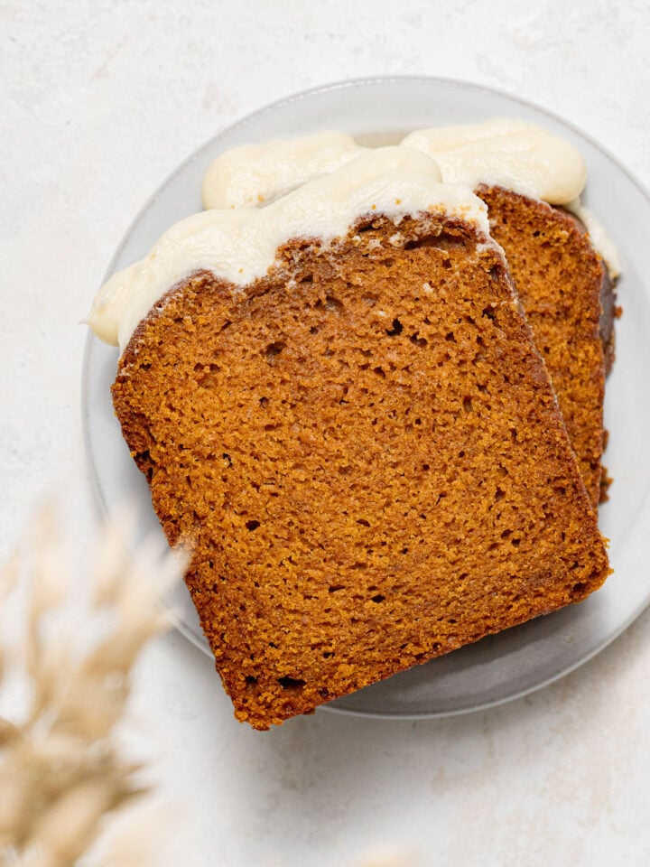 two slices of pumpkin bread with cream cheese frosting on small plate.