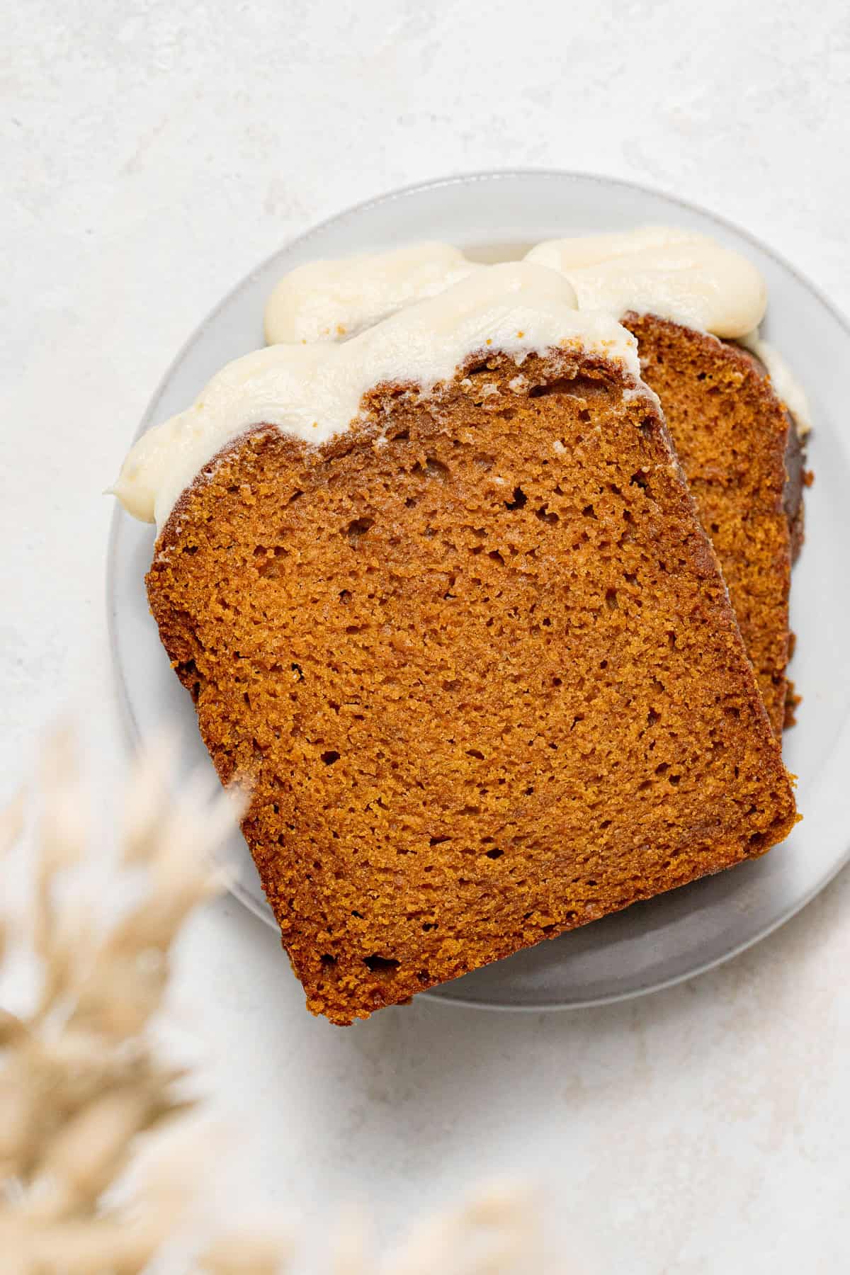 two slices of pumpkin bread with cream cheese frosting on small plate.