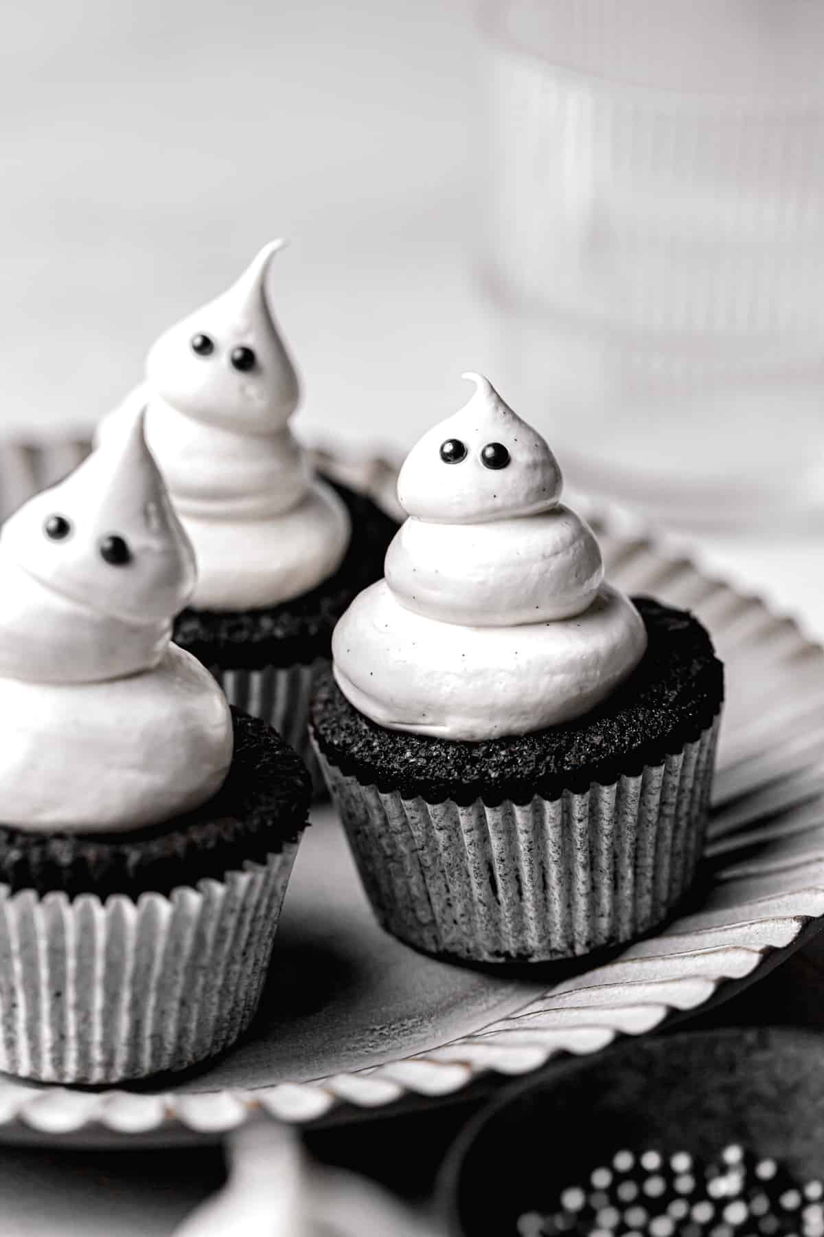 black cocoa cupcakes with meringue ghosts on grey plate.