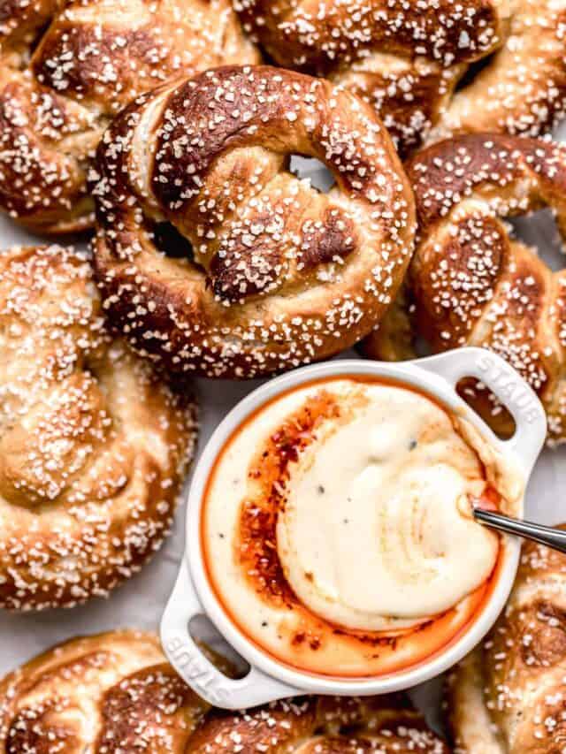 soft pretzels piled on baking sheet with bowl of cheese dip