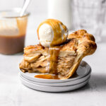 slice of salted caramel apple pie on stacked plates with scoop of ice cream and caramel drizzle