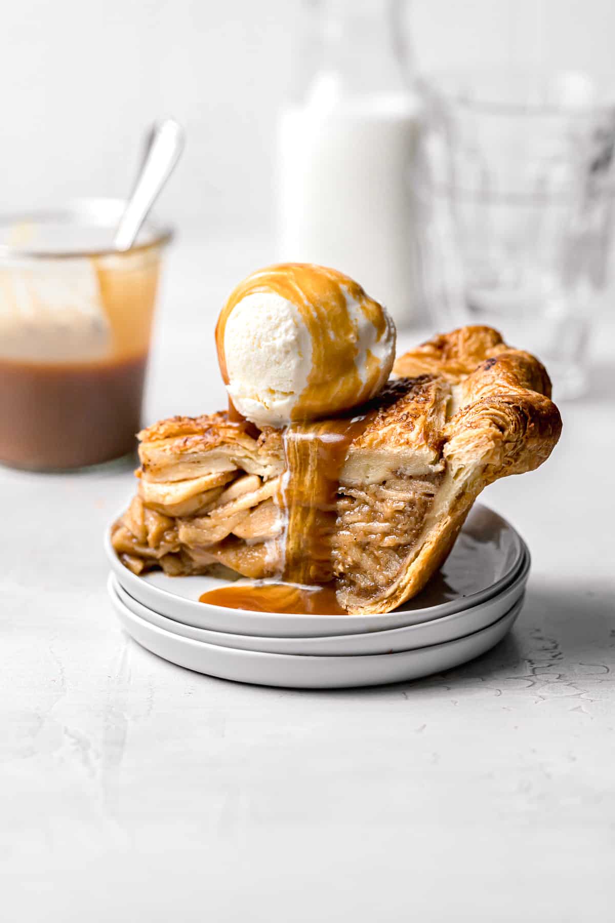 slice of salted caramel apple pie on stacked plates with scoop of ice cream and caramel drizzle.