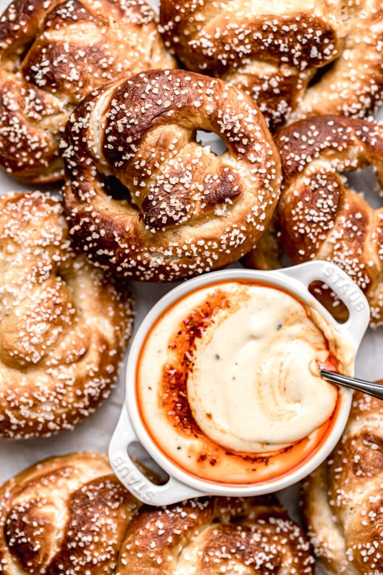 soft pretzels piled on baking sheet with bowl of cheese dip