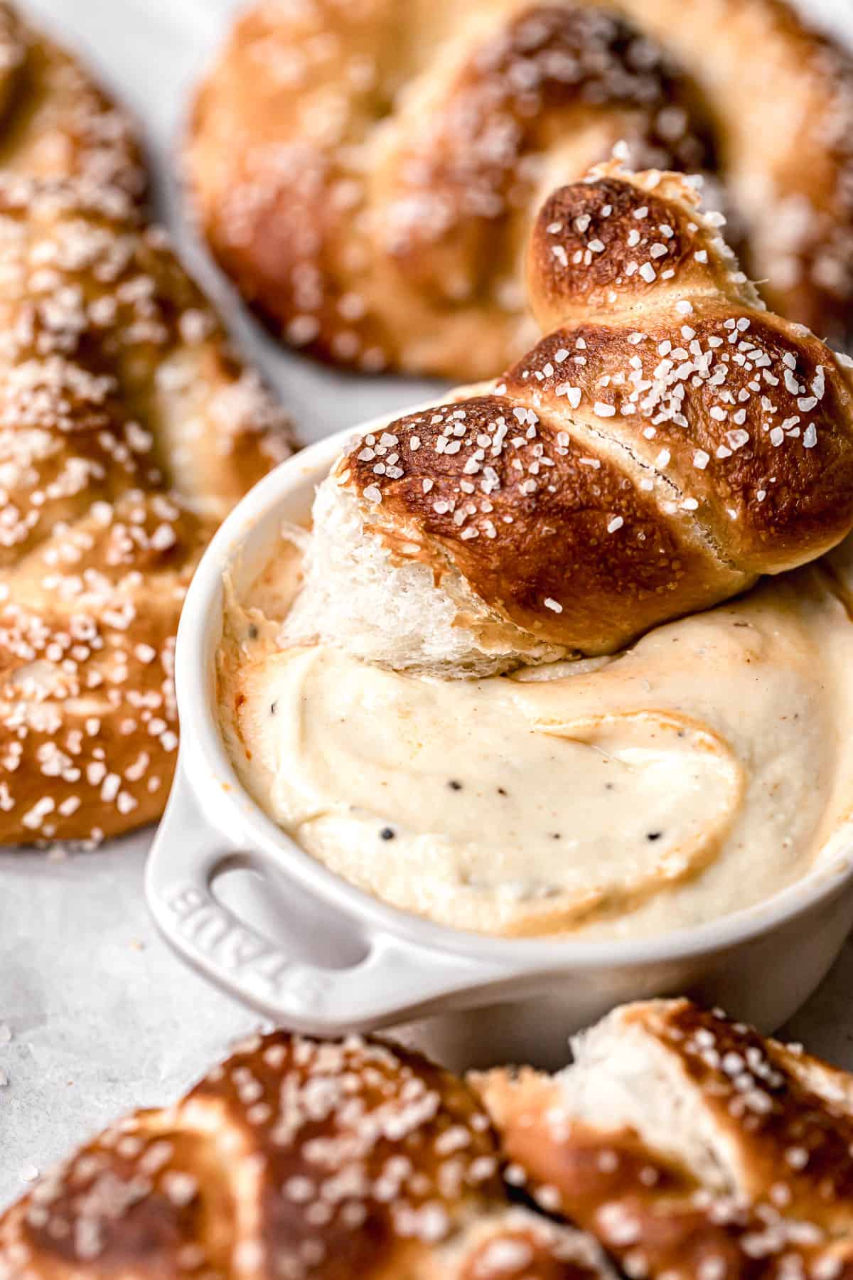 close up of small bowl of cheese dip with a bite of a soft pretzel on top.