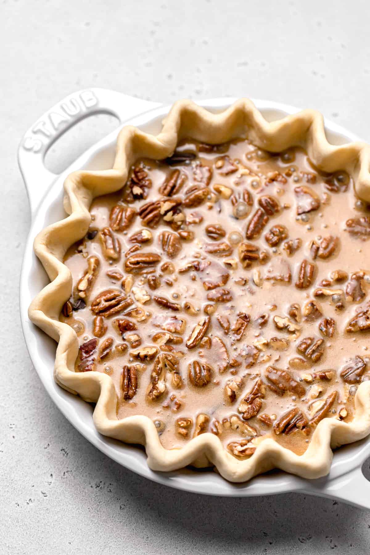 caramel filling poured over pecans and chocolate chips in pie dough
