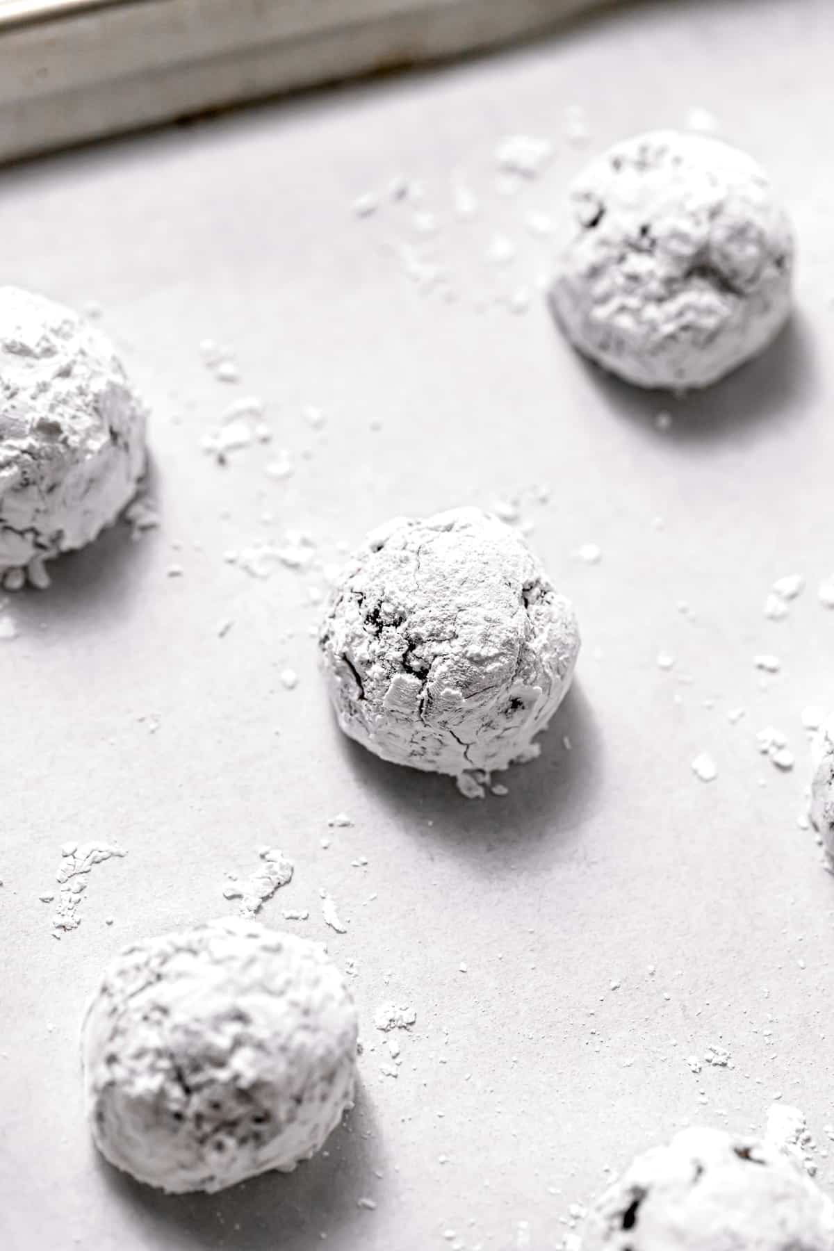 cookie dough balls rolled in powdered sugar on baking sheet.