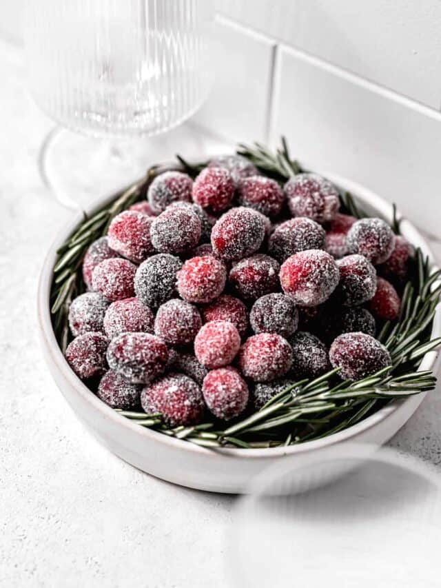 sugared cranberries in white bowl with rosemary