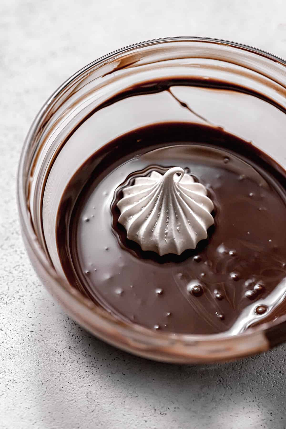 one meringue cookie in bowl of melted chocolate.