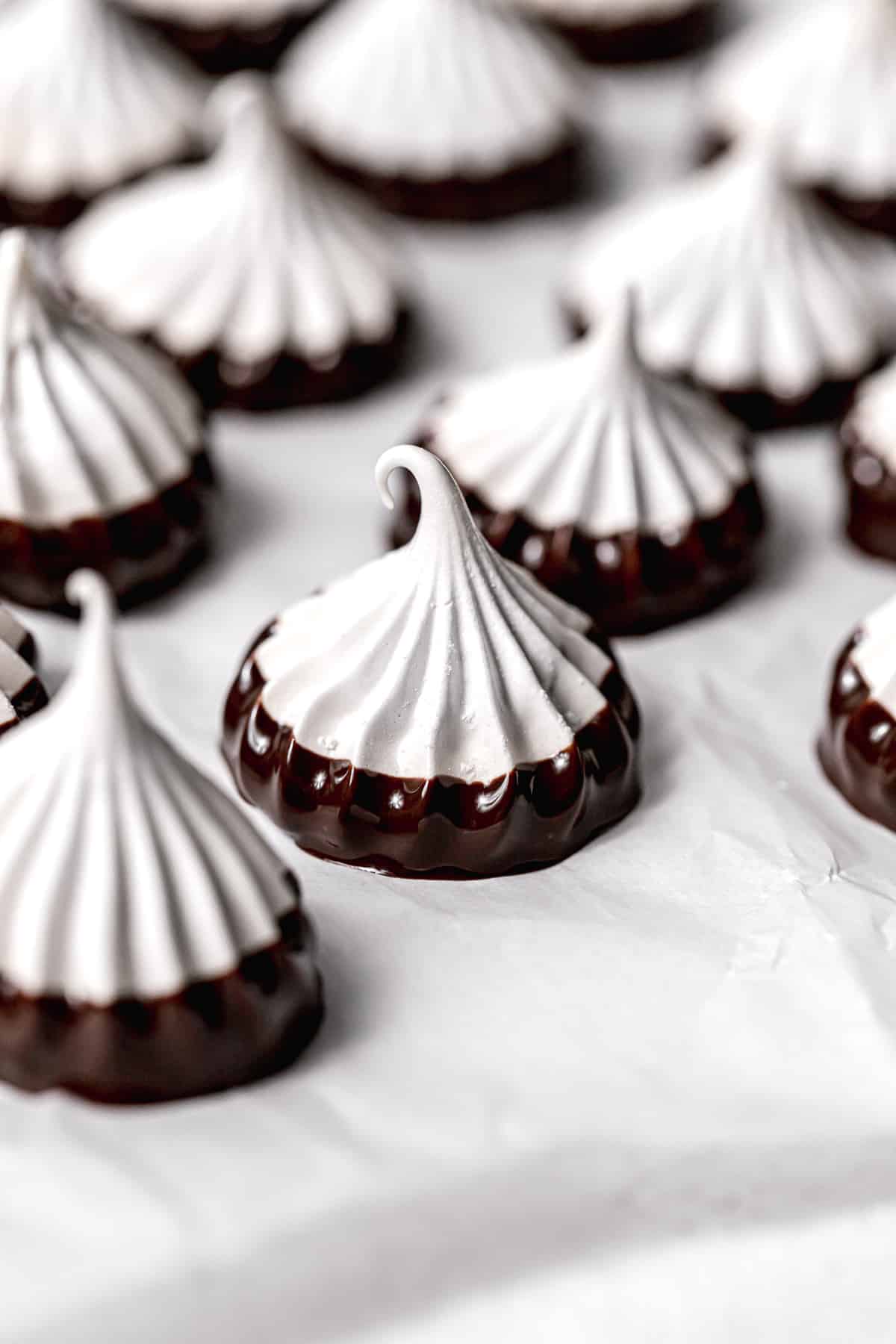 meringue cookies dipped in chocolate on parchment paper.