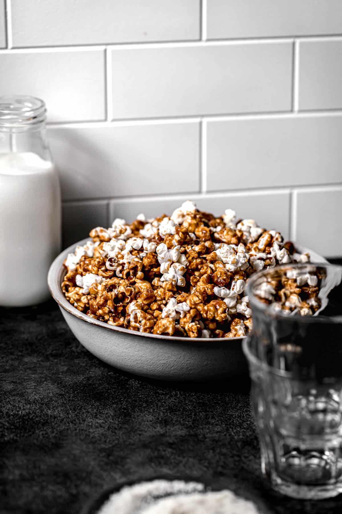 homemade caramel popcorn in large bowl next to jug of milk.