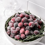 sugared cranberries in white bowl with rosemary