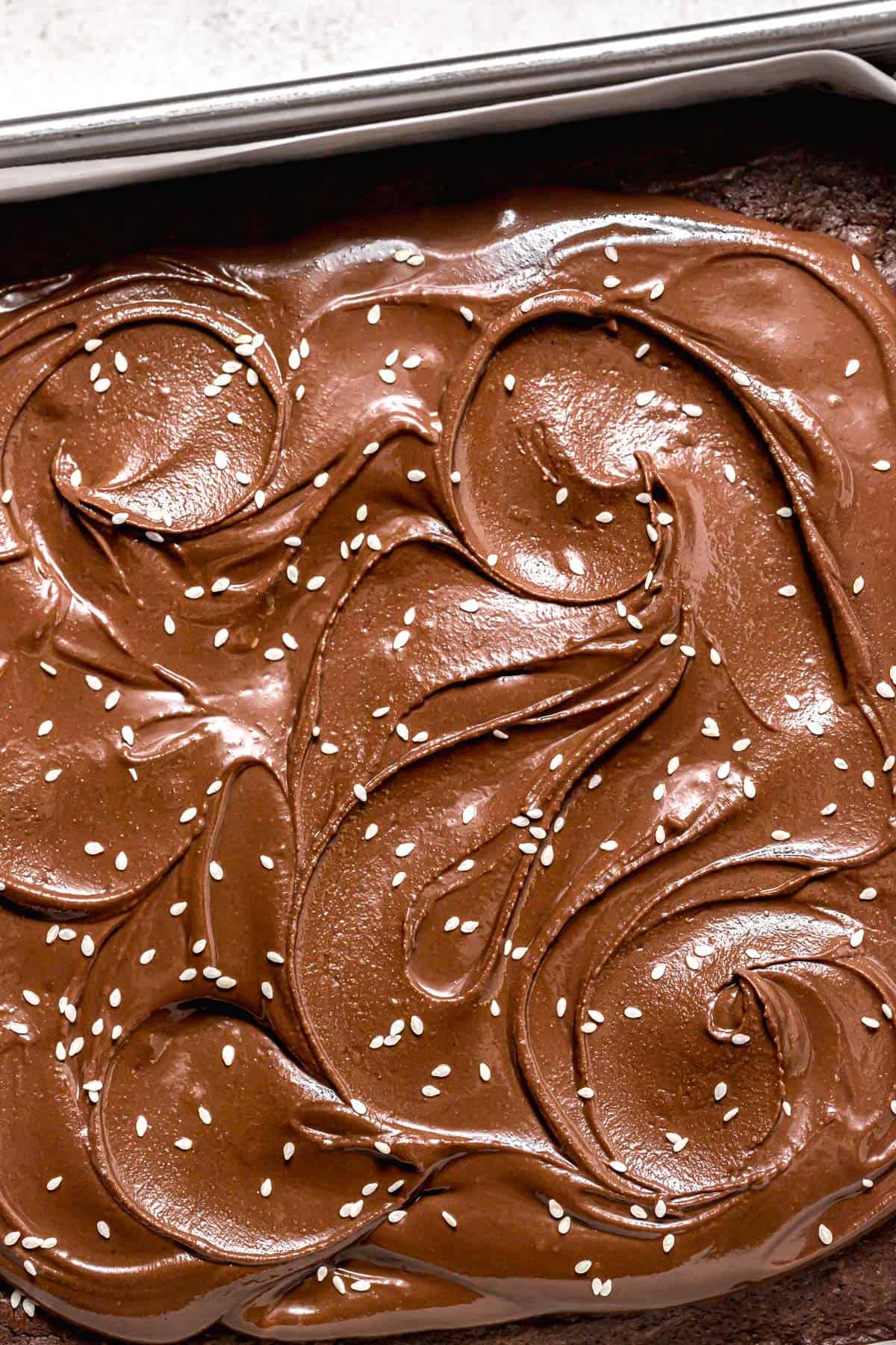 chocolate tahini frosting spread on brownies in square pan.
