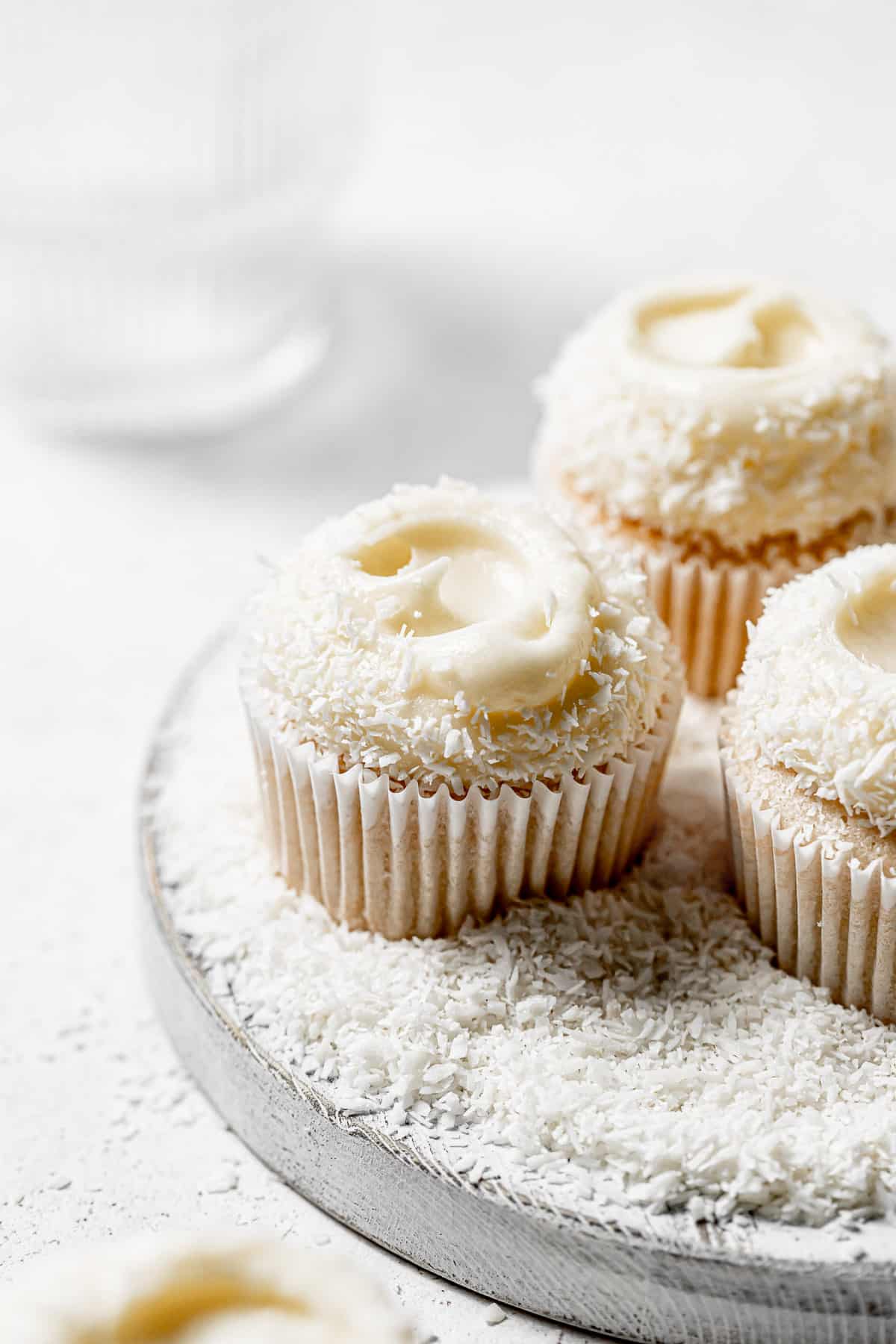 coconut cupcakes on white wooden board covered in coconut flakes. 