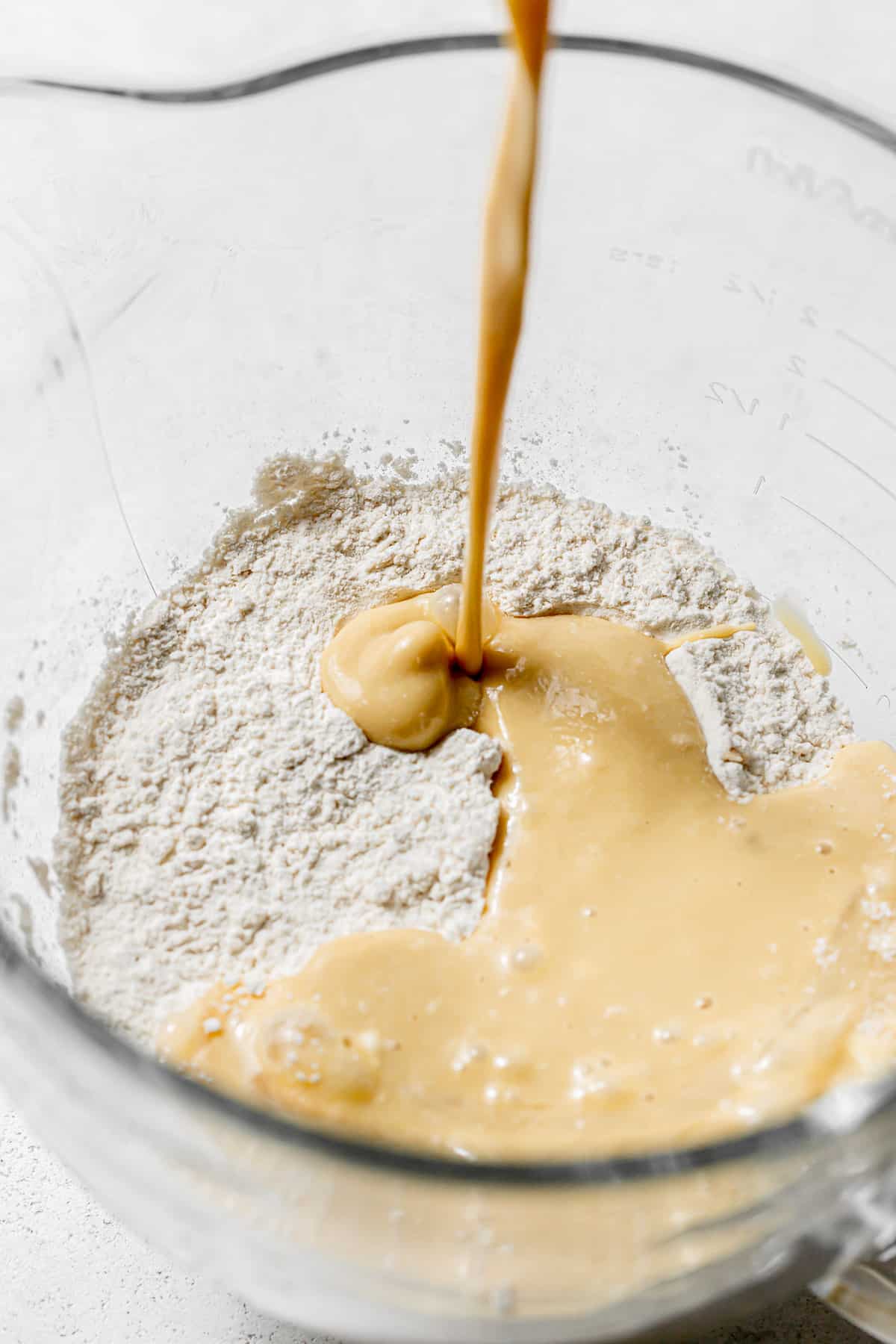 egg mixture being poured into flour in glass mixing bowl.