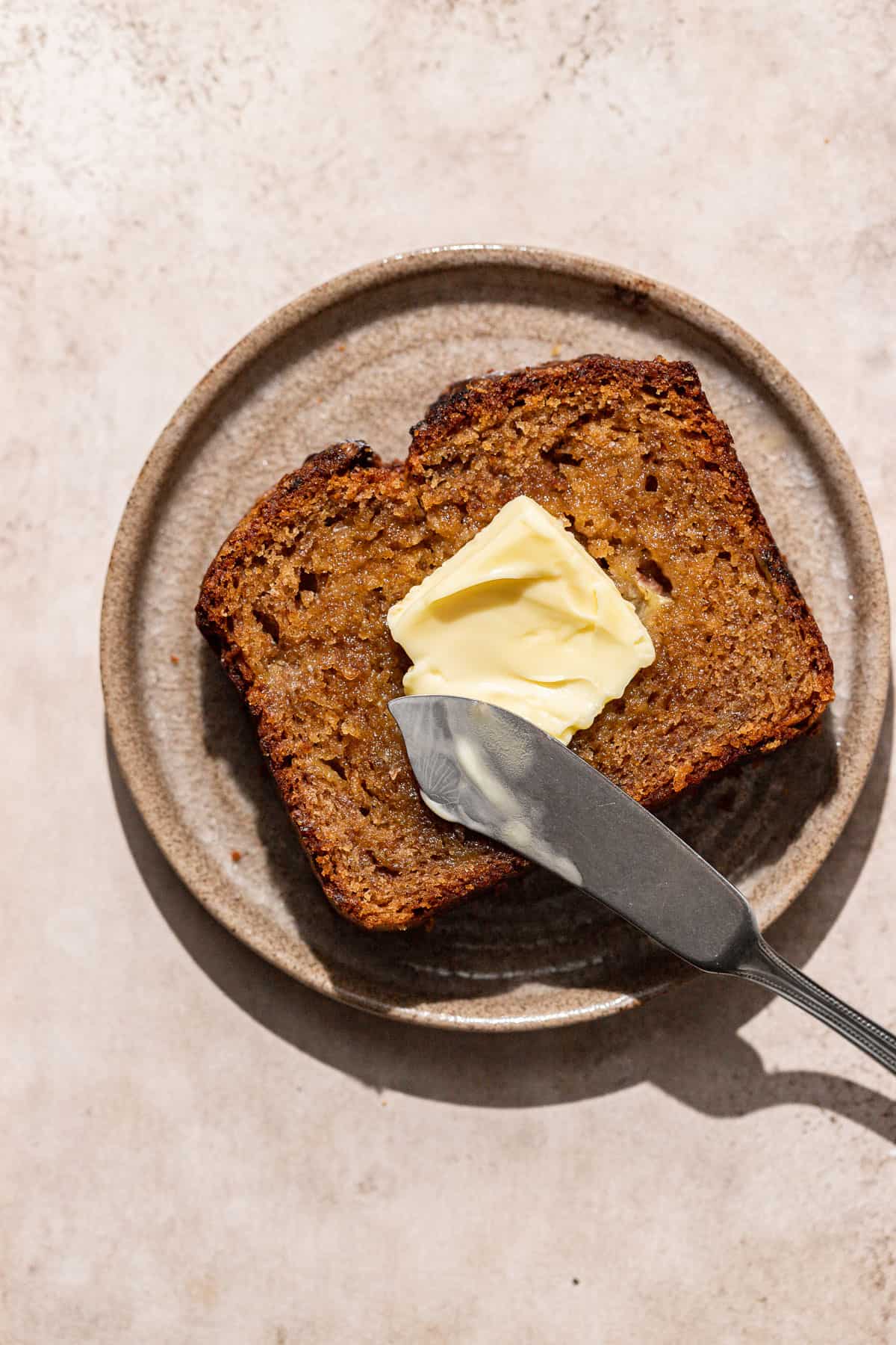 slice of brown butter banana bread on plate with pat of butter. 