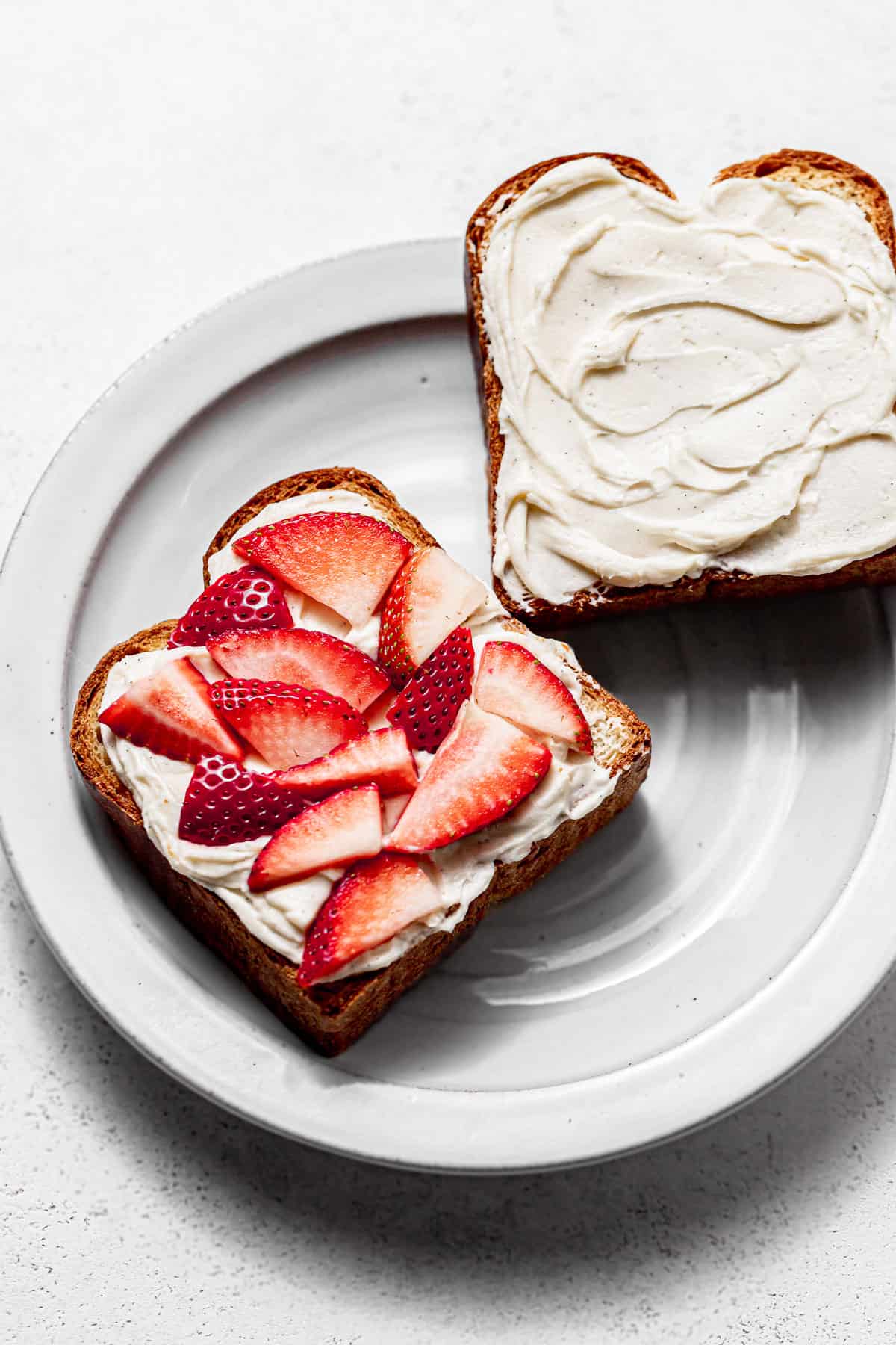 brioche bread slices covered with cream cheese filling and topped with strawberries on white plate.