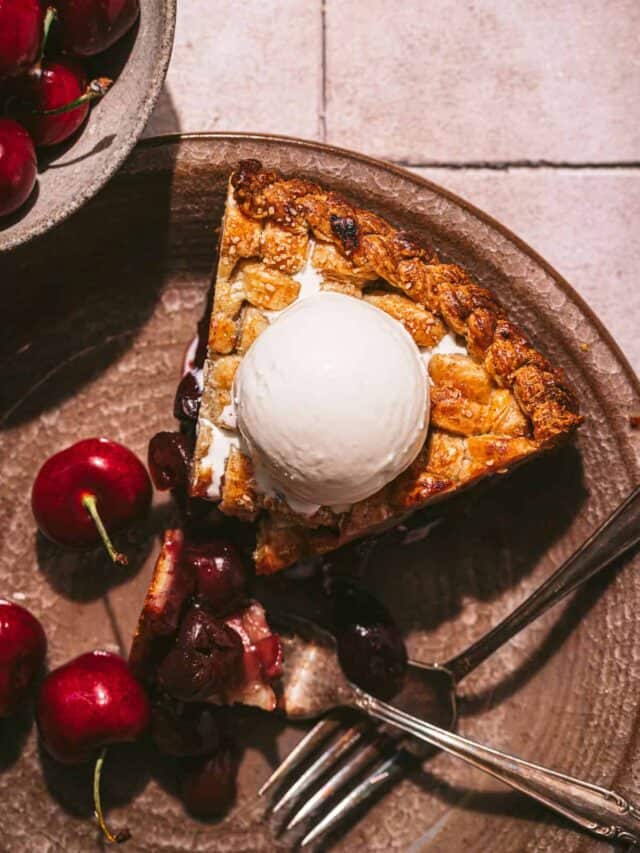 slice of cherry pie topped with vanilla ice cream on plate.