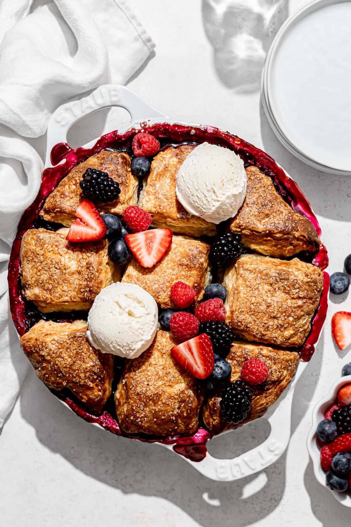 baked mixed berry cobbler with fresh fruit and ice cream on top.
