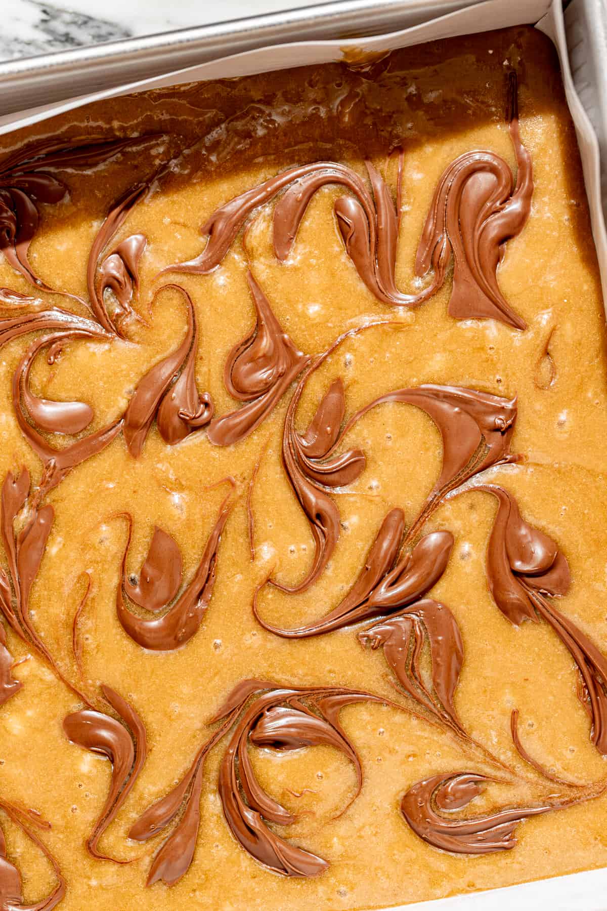 banana blondie batter in baking pan with Nutella swirled on top.