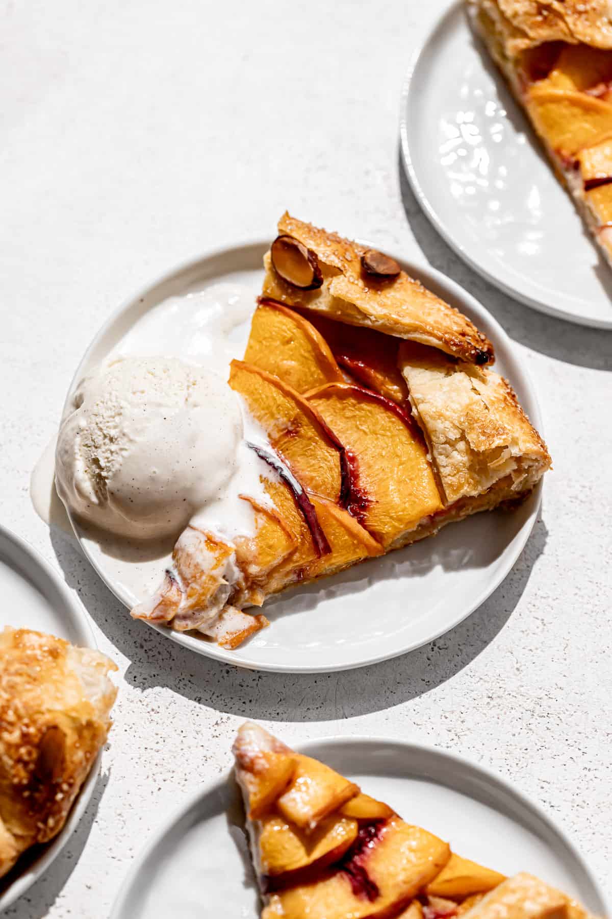 slice of almond peach galette on a white plate with a scoop of vanilla ice cream.