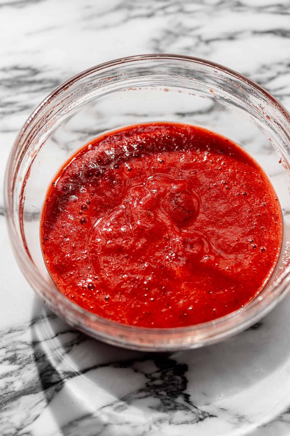 bowl of blended strawberry puree on a white marble background.