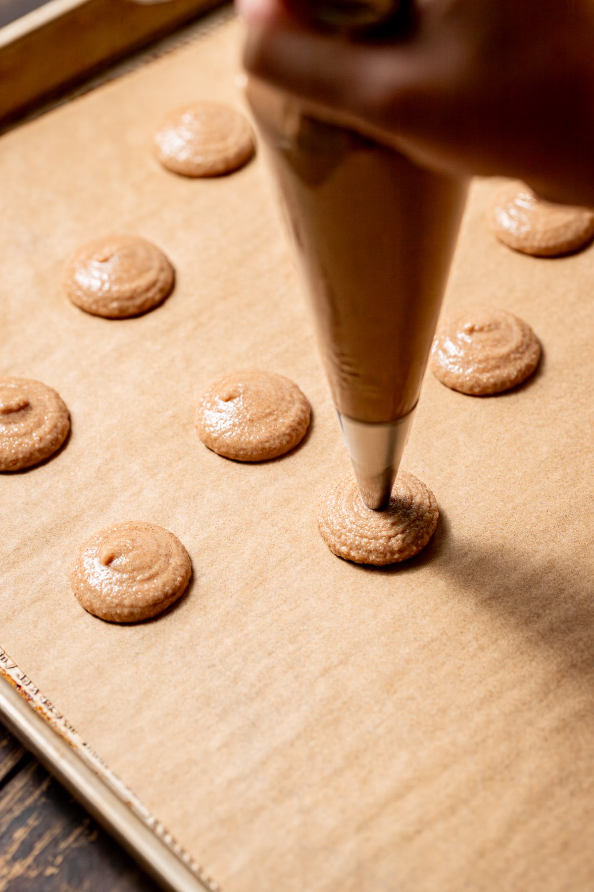 macaron batter being piped onto baking tray.
