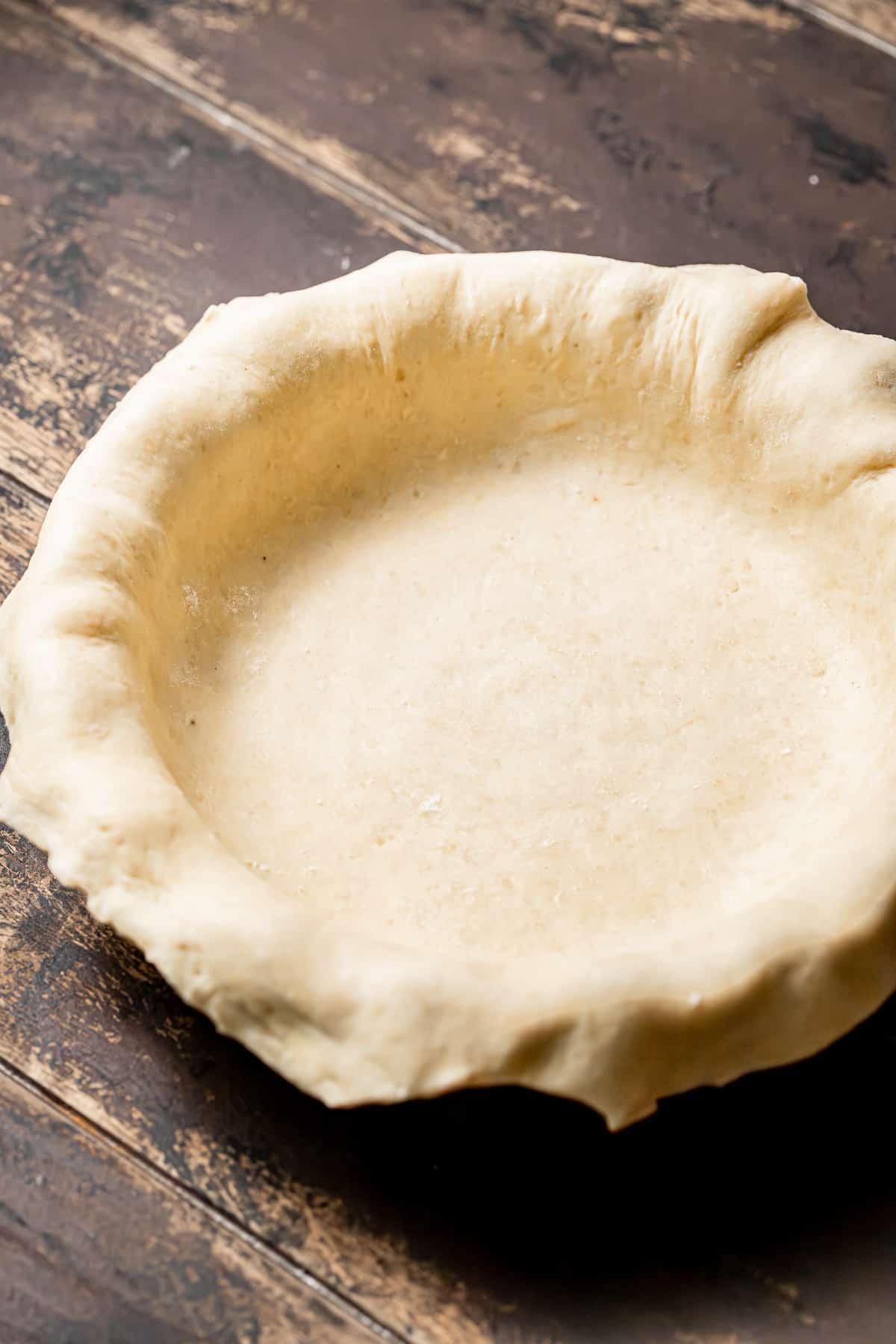 pie crust rolled over pie pan on wooden background.