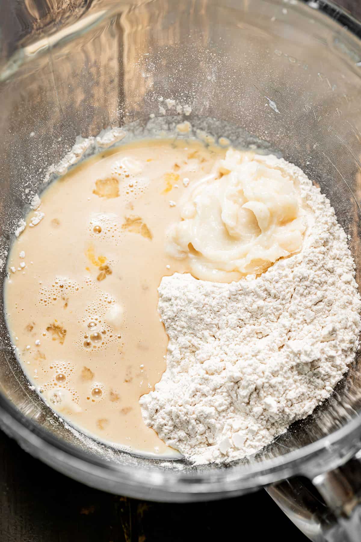wet and dry ingredients for bun dough in a glass bowl.