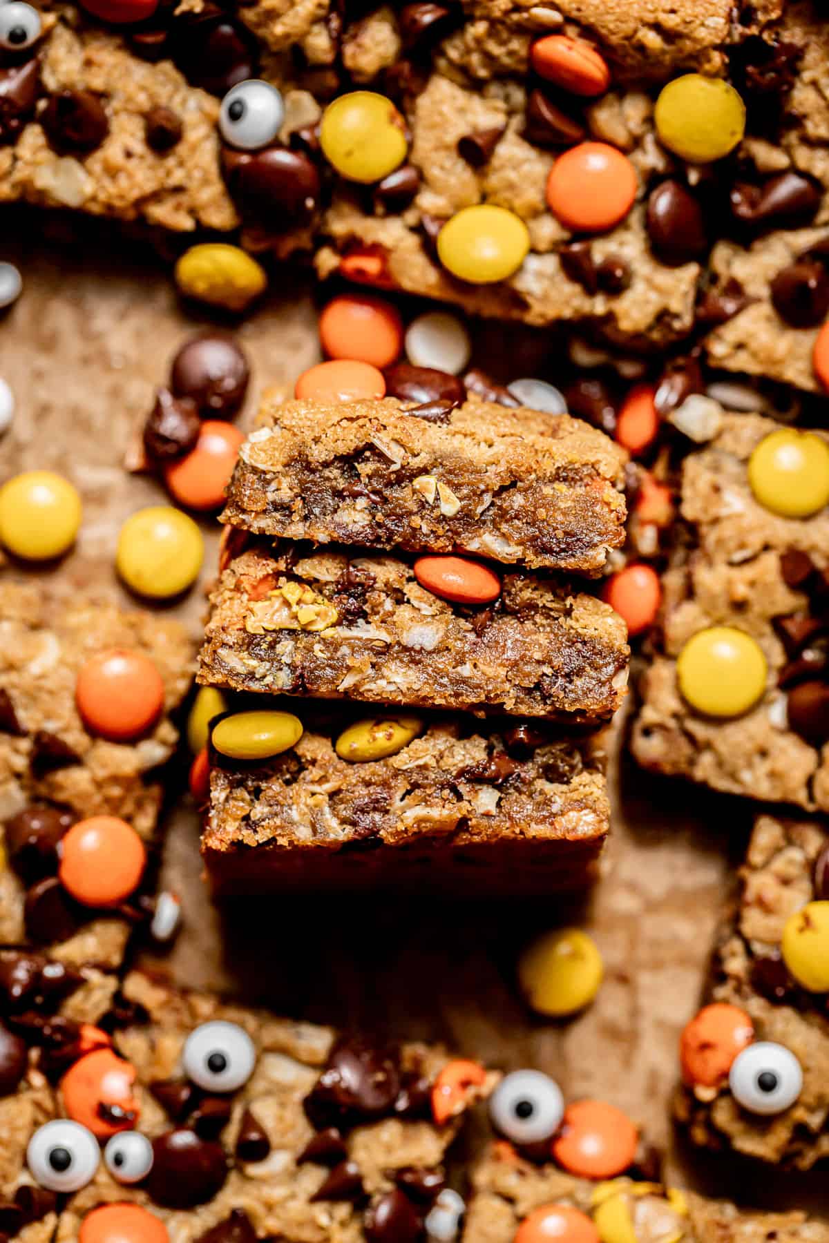 monster cookie bars on parchment paper with three stacked on their sides.