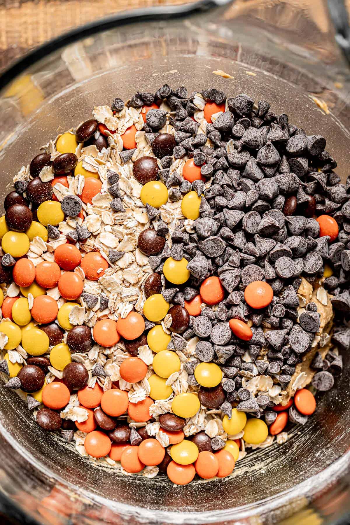 chocolate, Reese's pieces, and oats added to cookie dough in bowl.