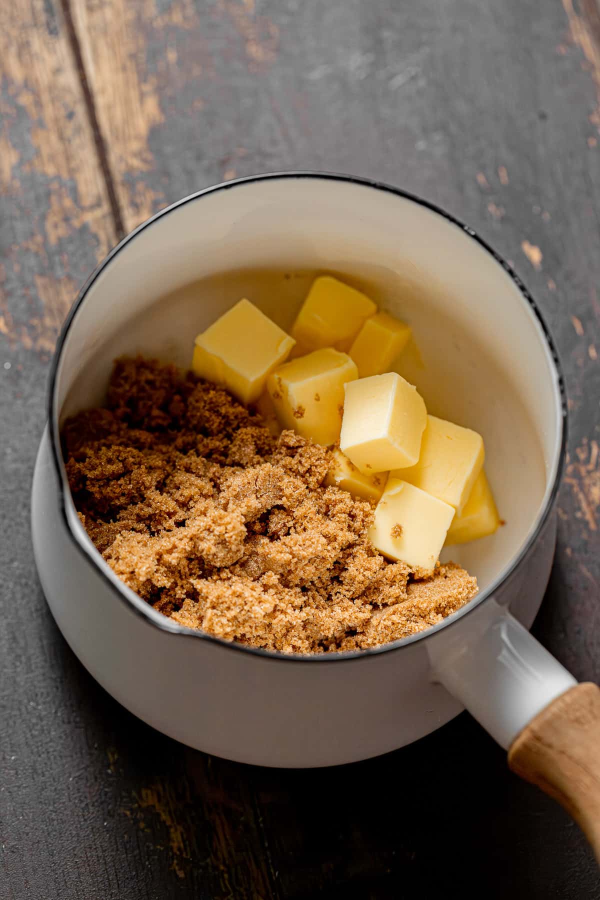 butter and brown sugar in saucepan on wooden background.