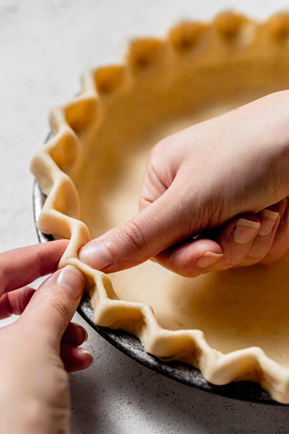 pie dough in metal pan being crimped. 