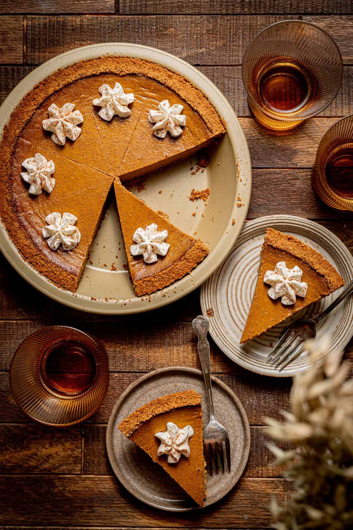 pumpkin pie with graham cracker crust in gold pie pan next to pieces of pie on plates.