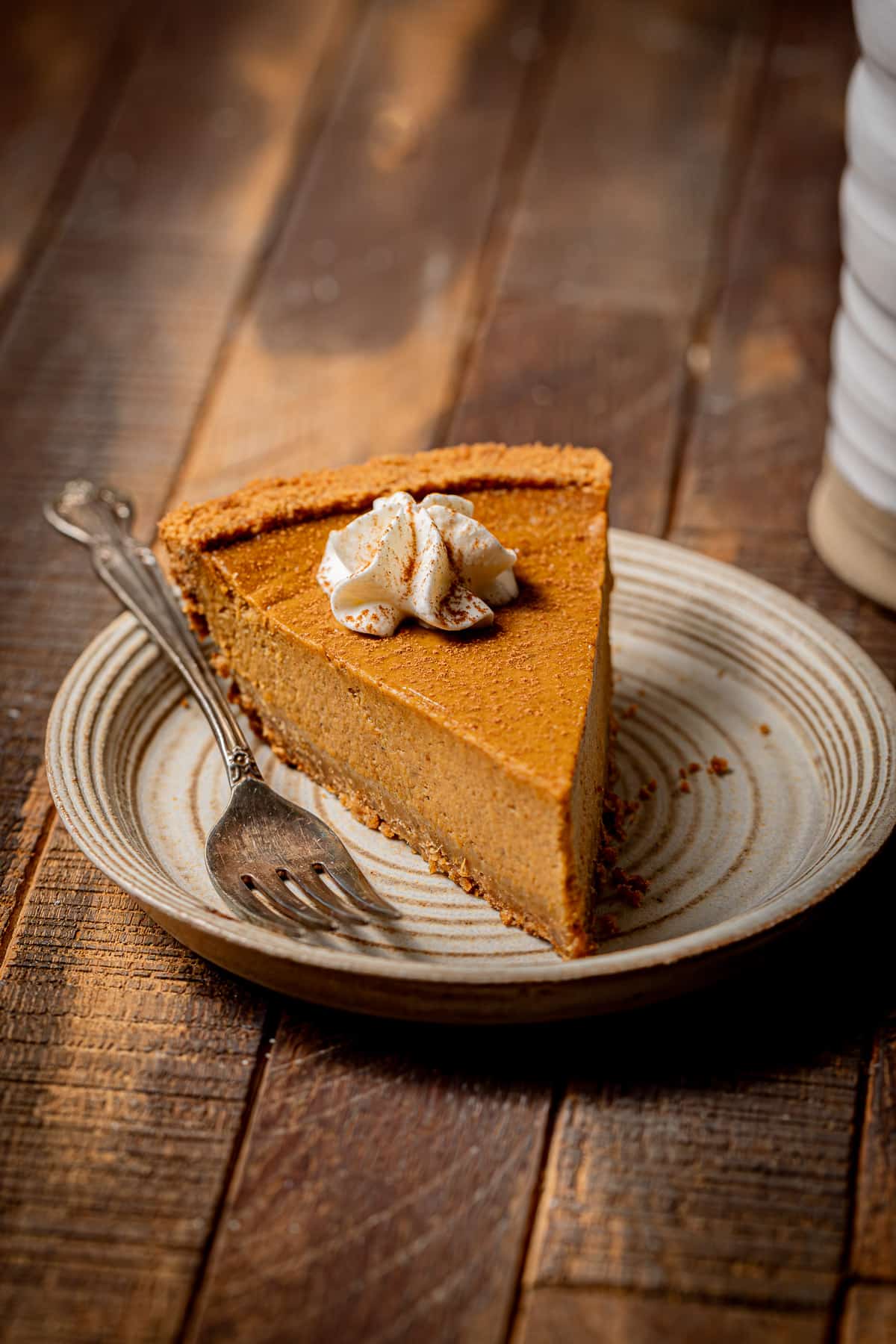 piece of pumpkin pie with graham cracker crust on plate with a fork.