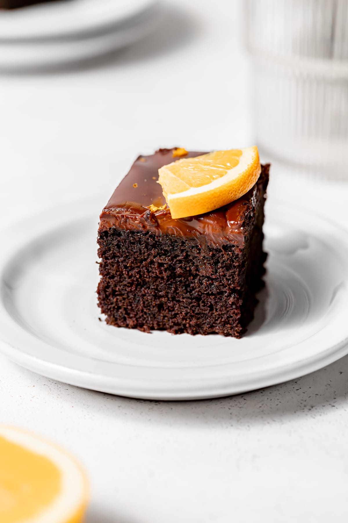 piece of chocolate orange cake on a white plate with an orange slice on top.