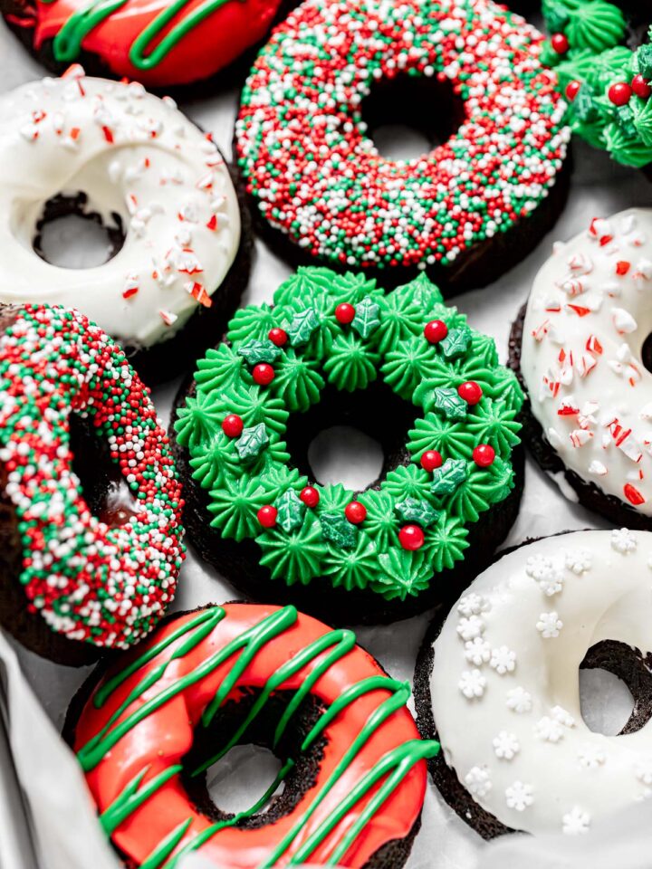chocolate peppermint Christmas donuts with various toppings lined up on parchment paper.