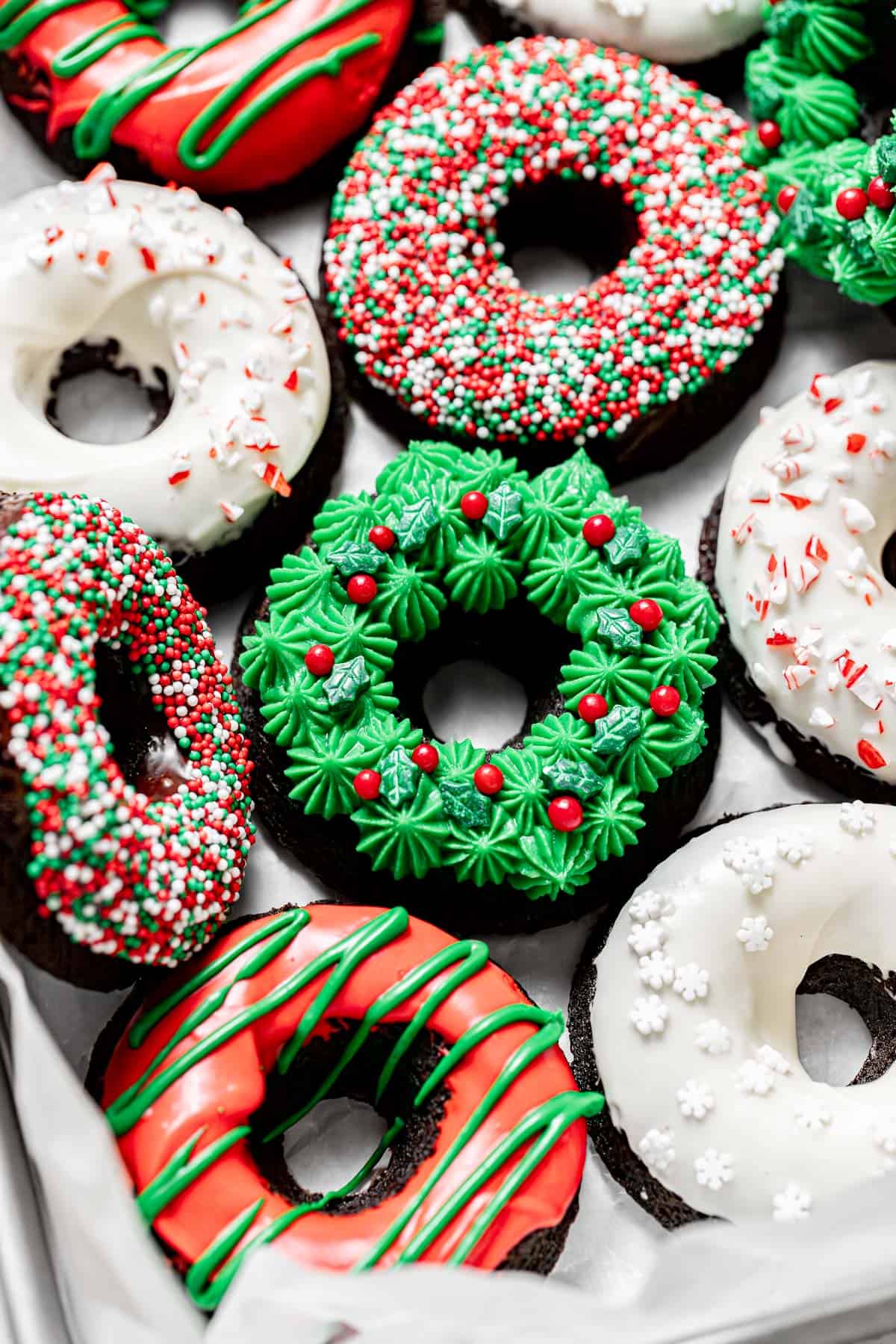 chocolate peppermint Christmas donuts with various toppings lined up on parchment paper.