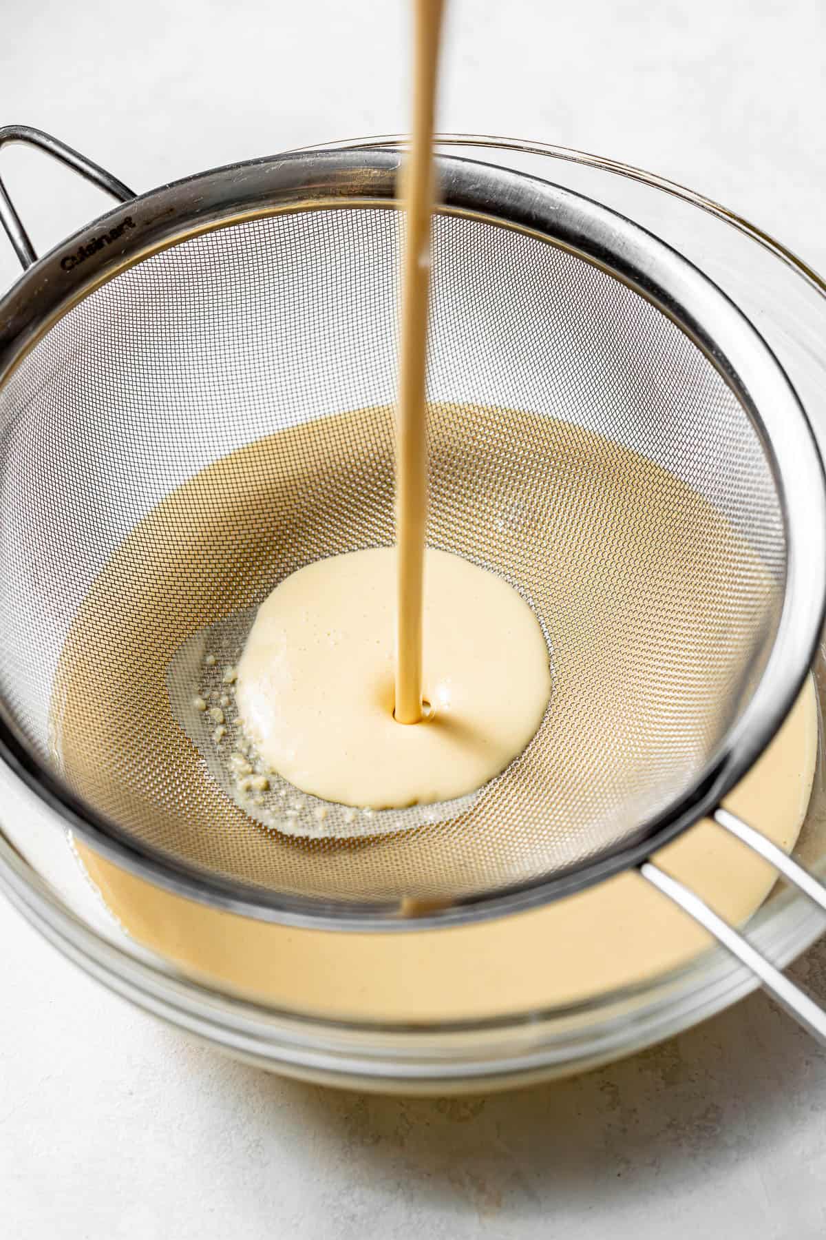 crepe batter poured through a sieve into a glass bowl.