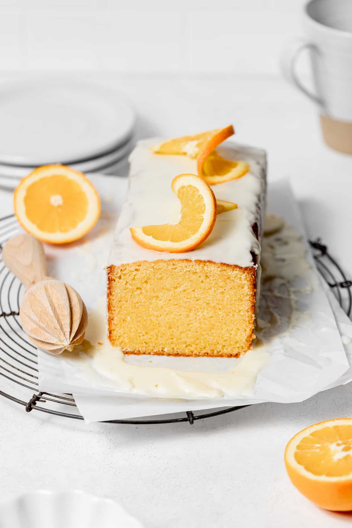 glazed orange pound cake with orange slices on top sitting on a wire rack with parchment paper.