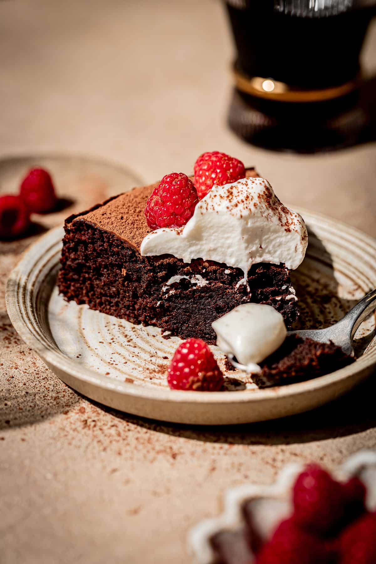 slice of red wine chocolate cake on small plate with whipped cream and fresh raspberries on top.
