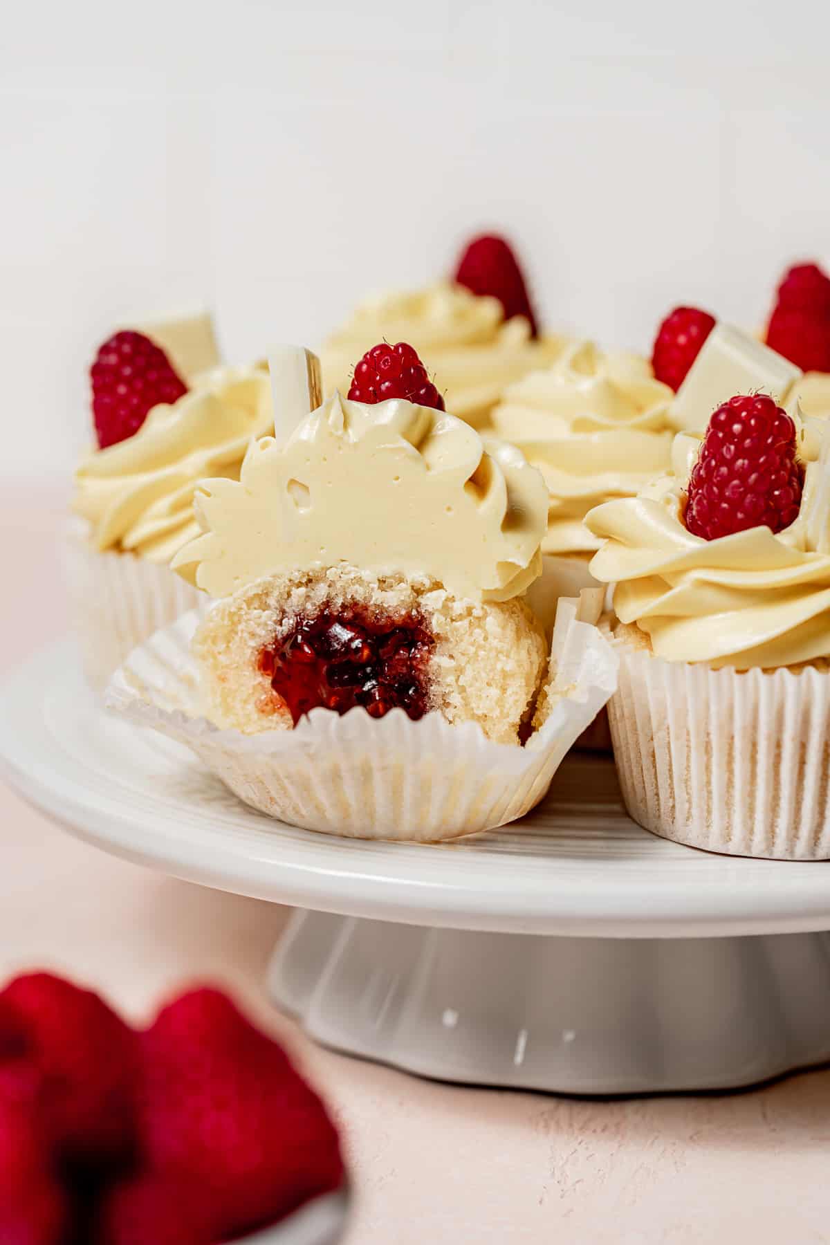 white chocolate raspberry cupcakes on white cake stand with one cut in half.