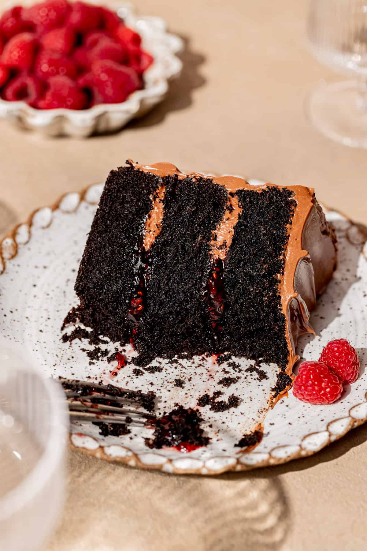 slice of dark chocolate raspberry cake on white plate with fork.