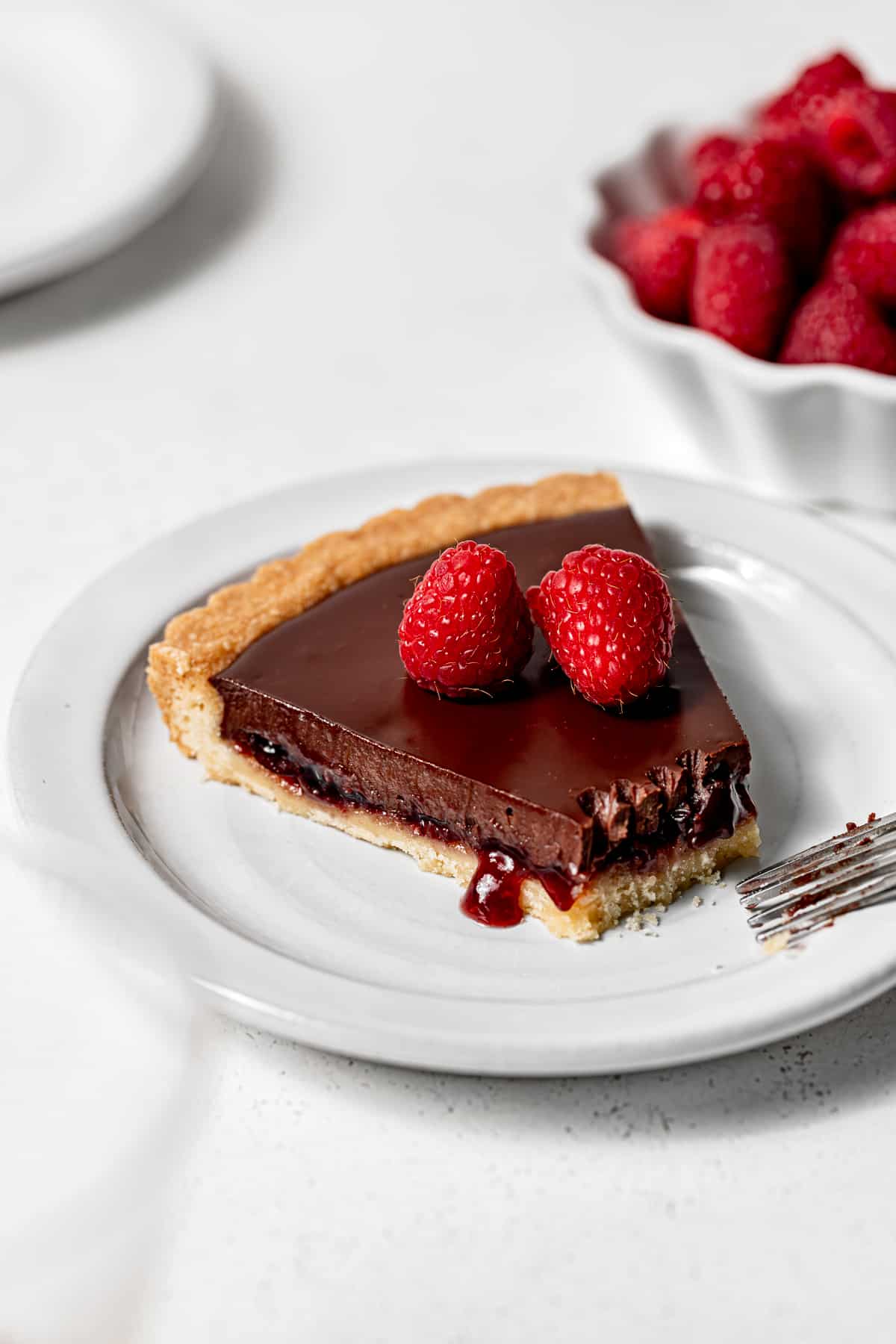 slice of raspberry chocolate tart on white plate.