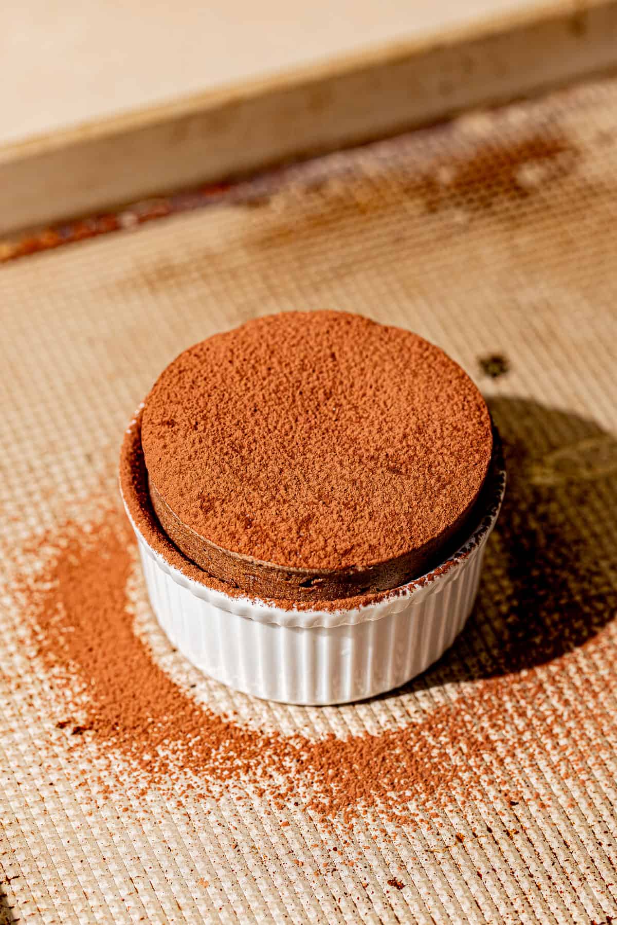 chocolate souffle in white ramekin with cocoa powder dusted on top.