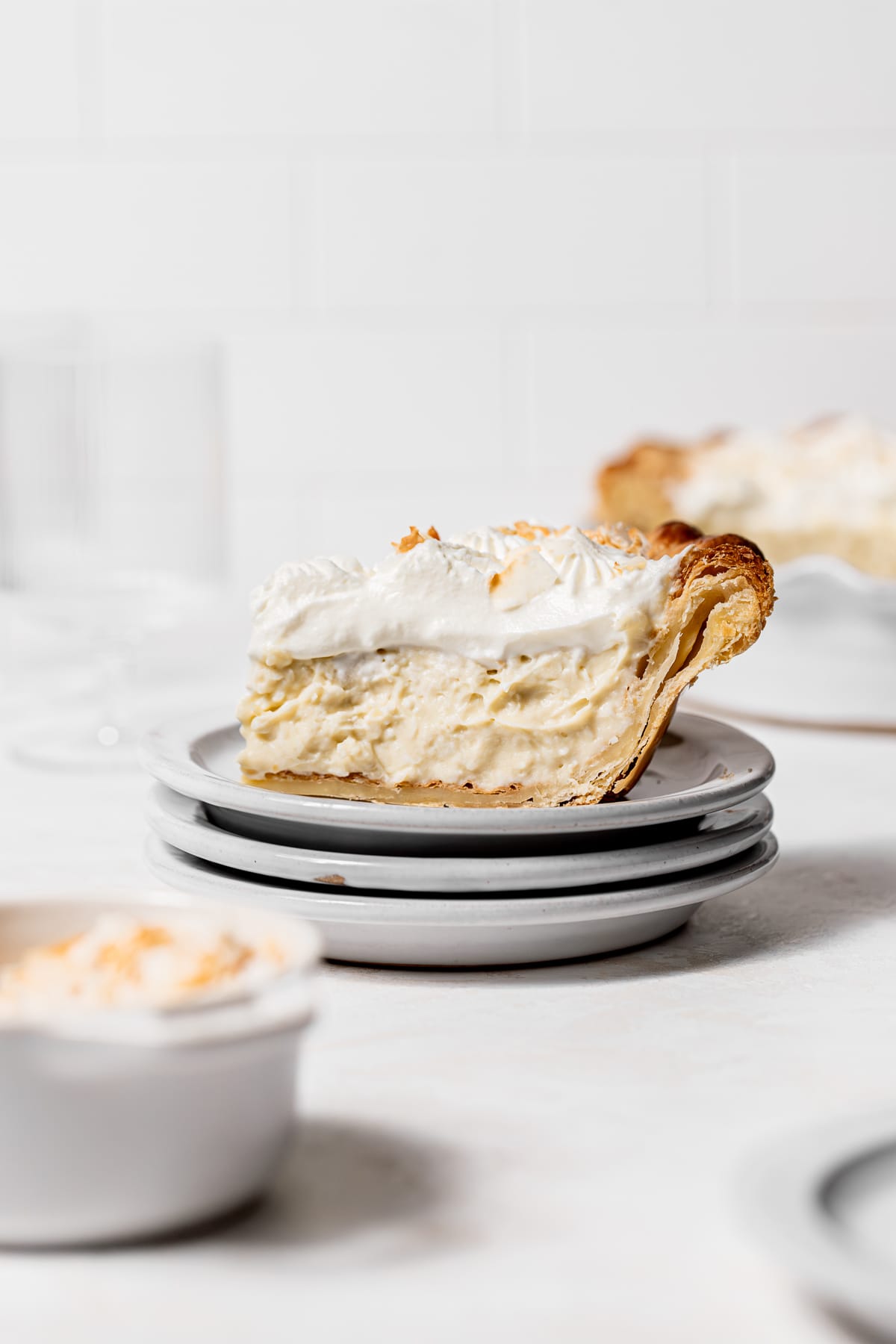 slice of deep dish coconut pie on three stacked white plates.